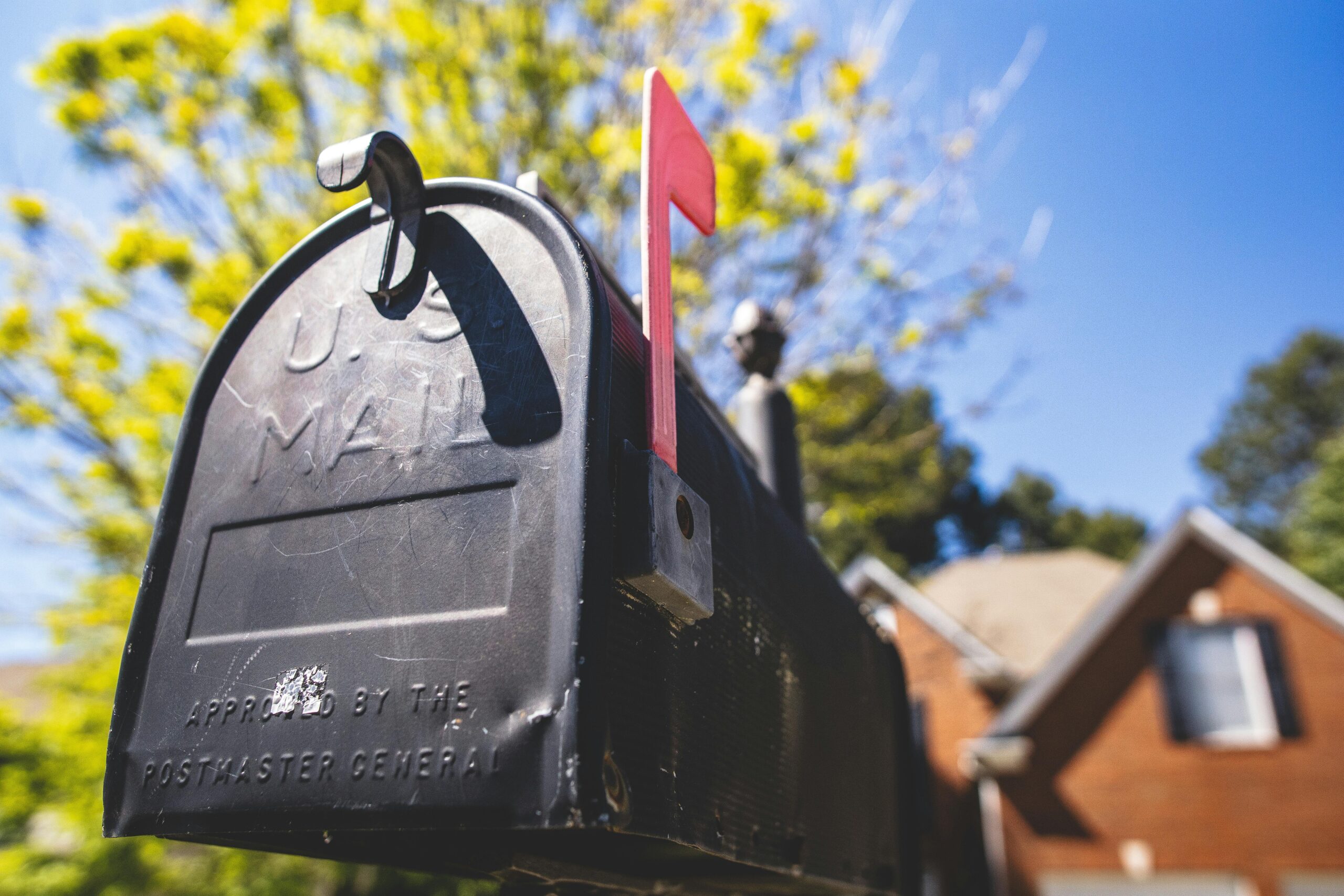 Close-up of a traditional US mailbox with a red flag in a sunny neighborhood.
